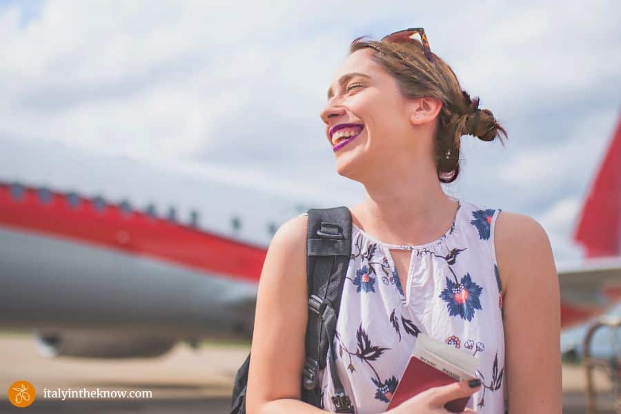 Smiling woman arriving at destination after a long flight with airplane in the background.